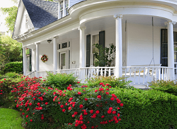 Nice older home with a wrap around porch and several well-maintained flower bushes and hedges in front